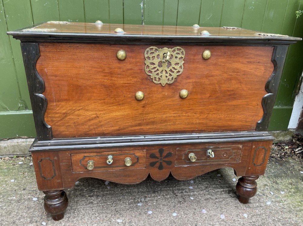 A 19th-century Dutch colonial teak and ebony chest with a pierced brass escutcheon, mounted on a two-drawer base with turned feet.