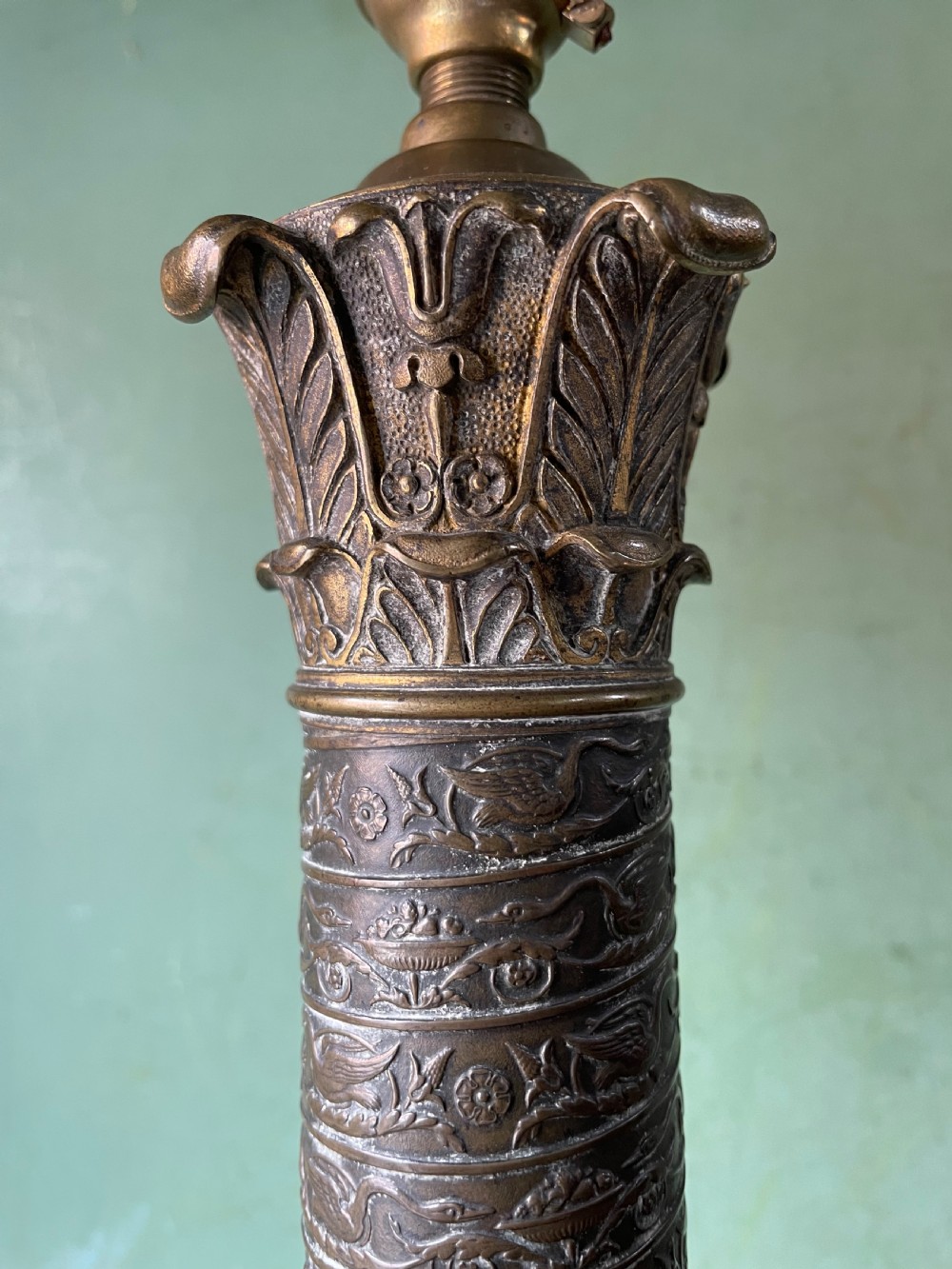 An early nineteenth-century patinated brass table lamp featuring a Corinthian capital, embossed shaft, and winged relief figure on a square stepped base. View VI