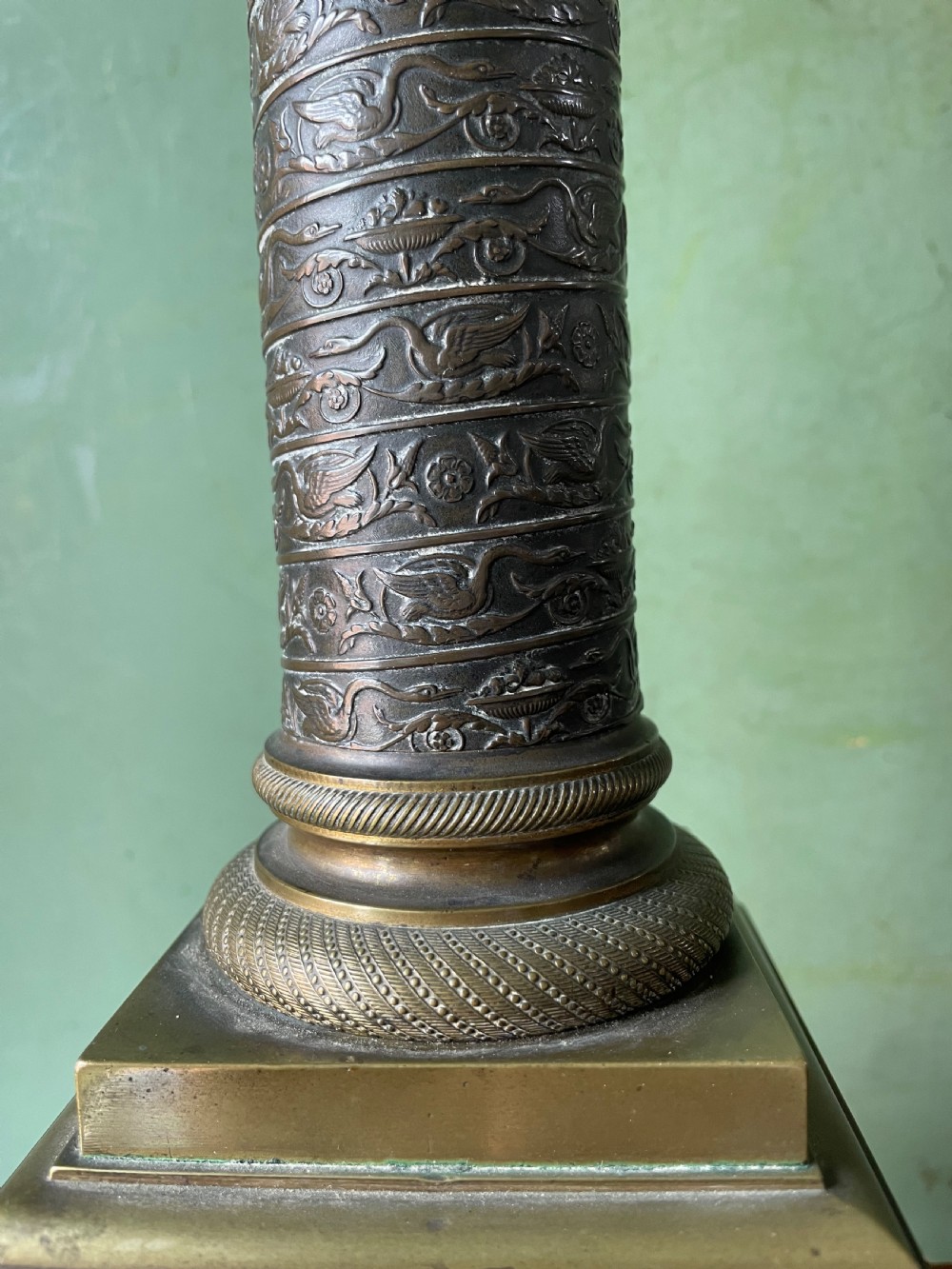 An early nineteenth-century patinated brass table lamp featuring a Corinthian capital, embossed shaft, and winged relief figure on a square stepped base. View VII