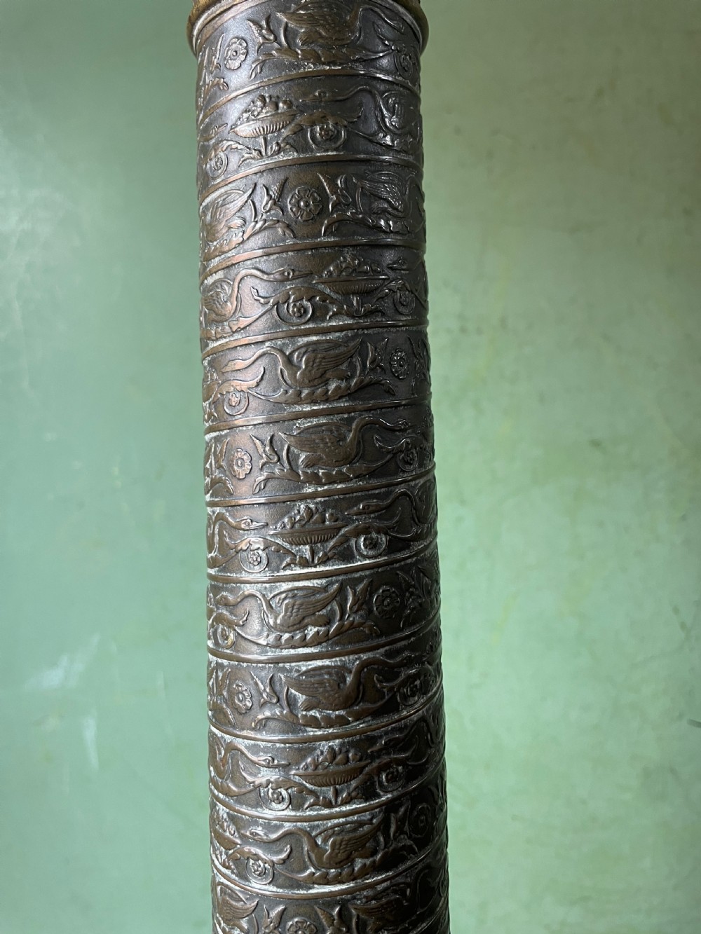 An early nineteenth-century patinated brass table lamp featuring a Corinthian capital, embossed shaft, and winged relief figure on a square stepped base. View IX