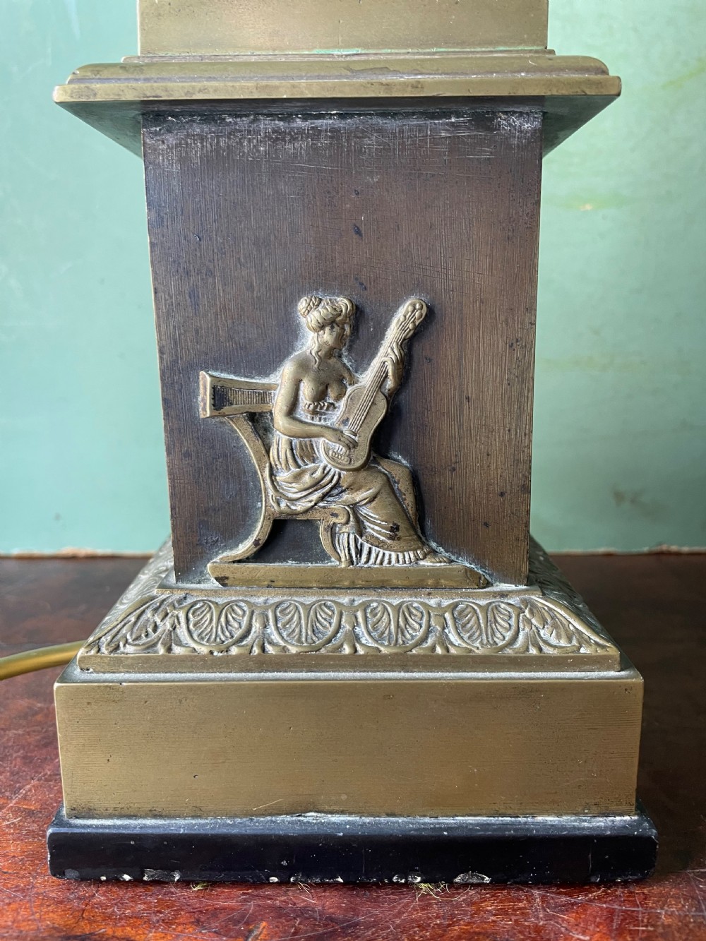 An early nineteenth-century patinated brass table lamp featuring a Corinthian capital, embossed shaft, and winged relief figure on a square stepped base. View X