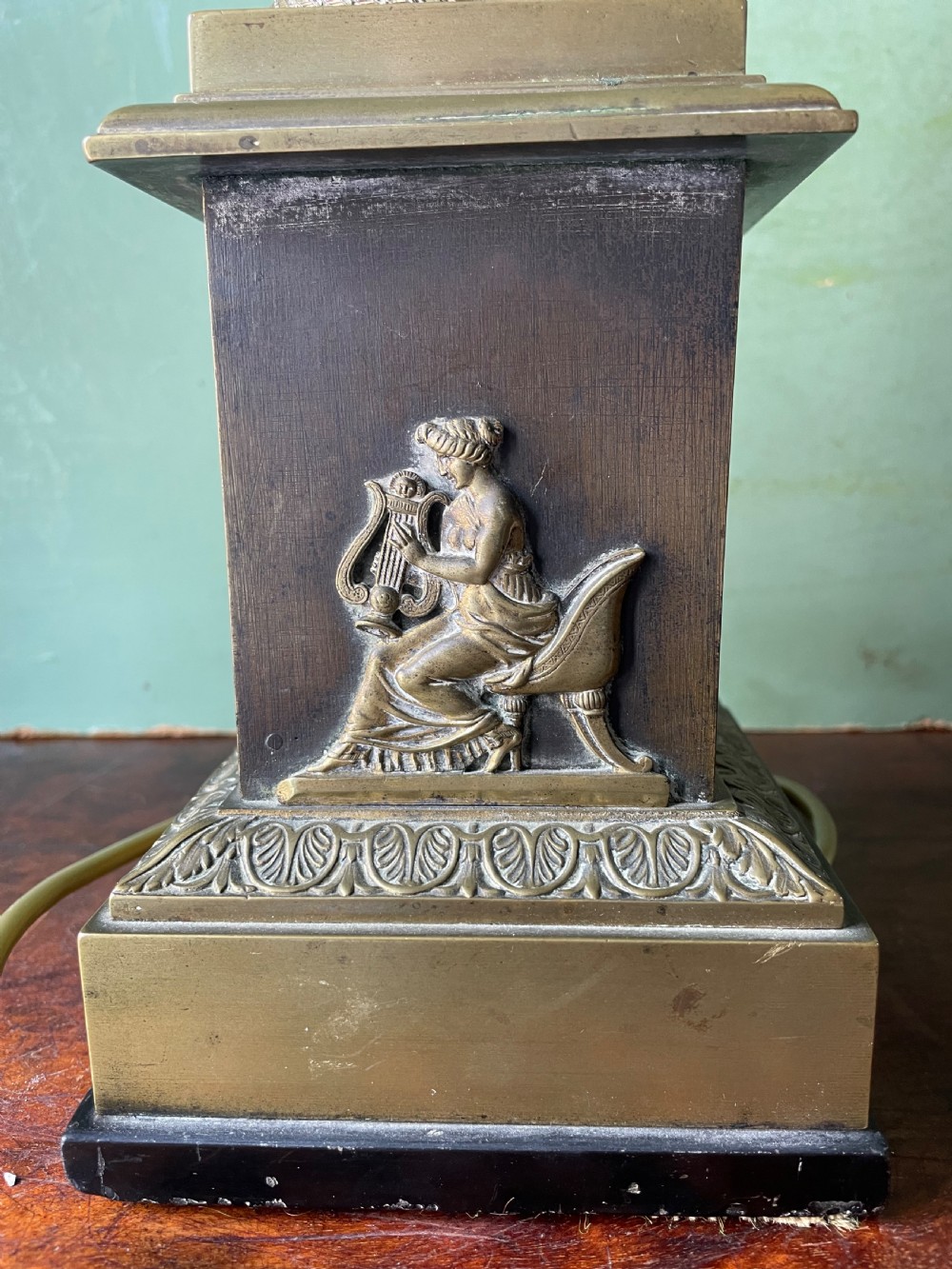 An early nineteenth-century patinated brass table lamp featuring a Corinthian capital, embossed shaft, and winged relief figure on a square stepped base. View XII