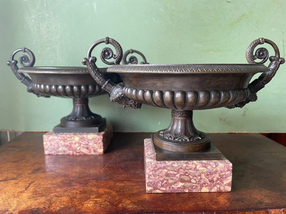 A pair of 19th-century dark bronze tazzas featuring gadrooned bowls and scroll handles, each mounted on a square red mottled marble base.