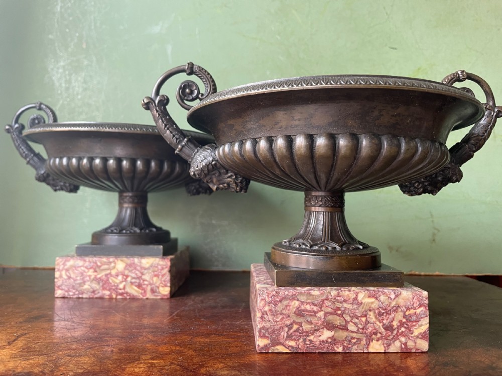A pair of 19th-century dark bronze tazzas featuring gadrooned bowls and scroll handles, each mounted on a square red mottled marble base. View II