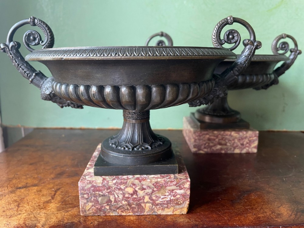 A pair of 19th-century dark bronze tazzas featuring gadrooned bowls and scroll handles, each mounted on a square red mottled marble base. View X