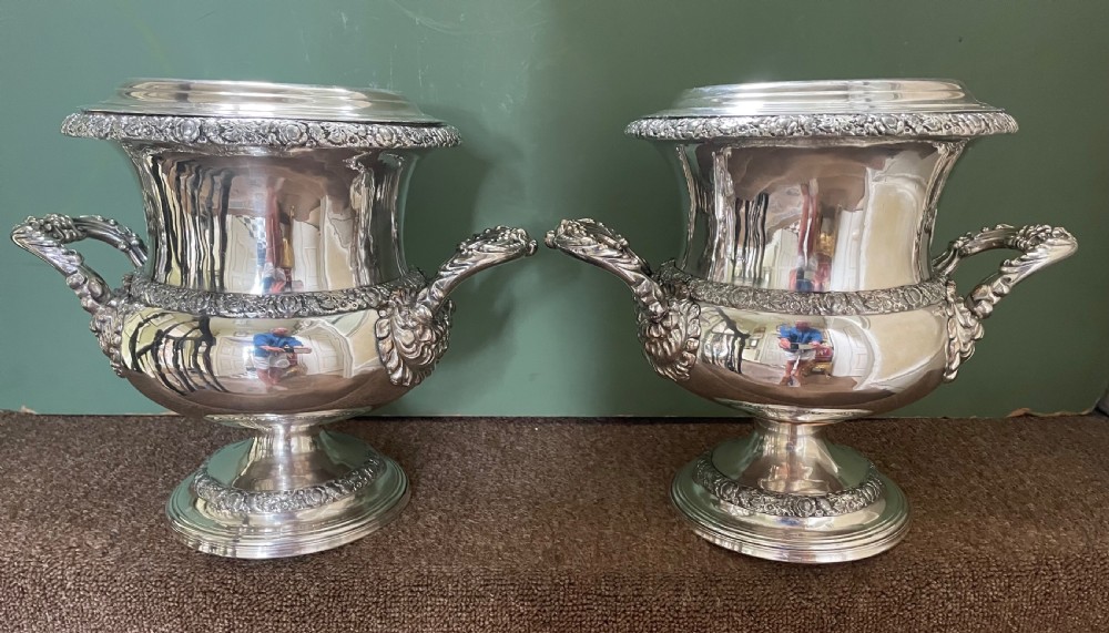 A pair of polished silver-plated campana-form wine coolers featuring ornate foliate handles, intricate relief borders, and pedestal bases. View II