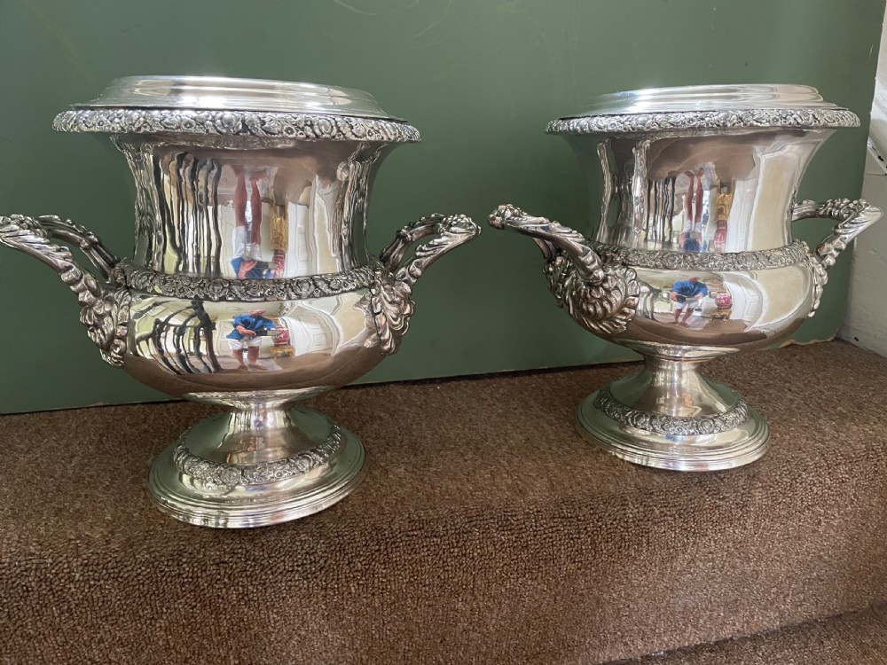 A pair of polished silver-plated campana-form wine coolers featuring ornate foliate handles, intricate relief borders, and pedestal bases. View III