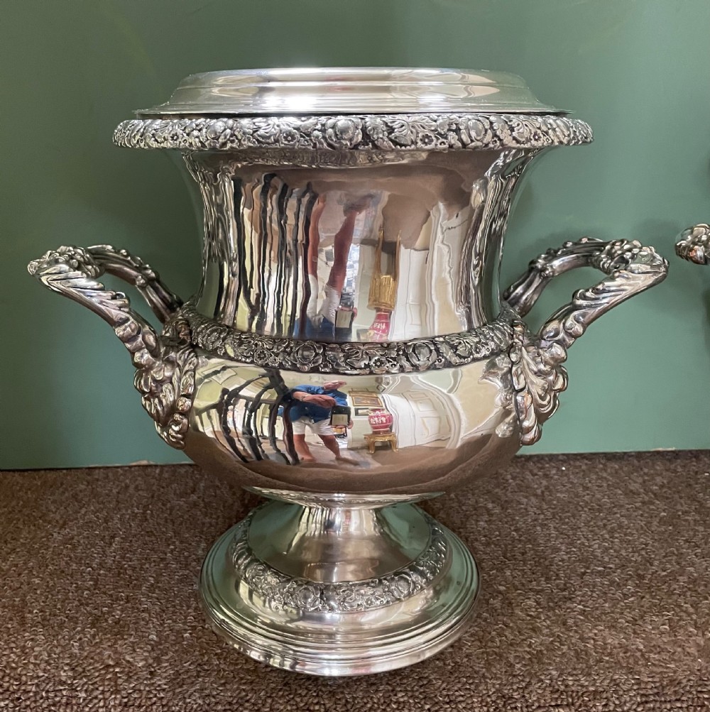 A pair of polished silver-plated campana-form wine coolers featuring ornate foliate handles, intricate relief borders, and pedestal bases. View V