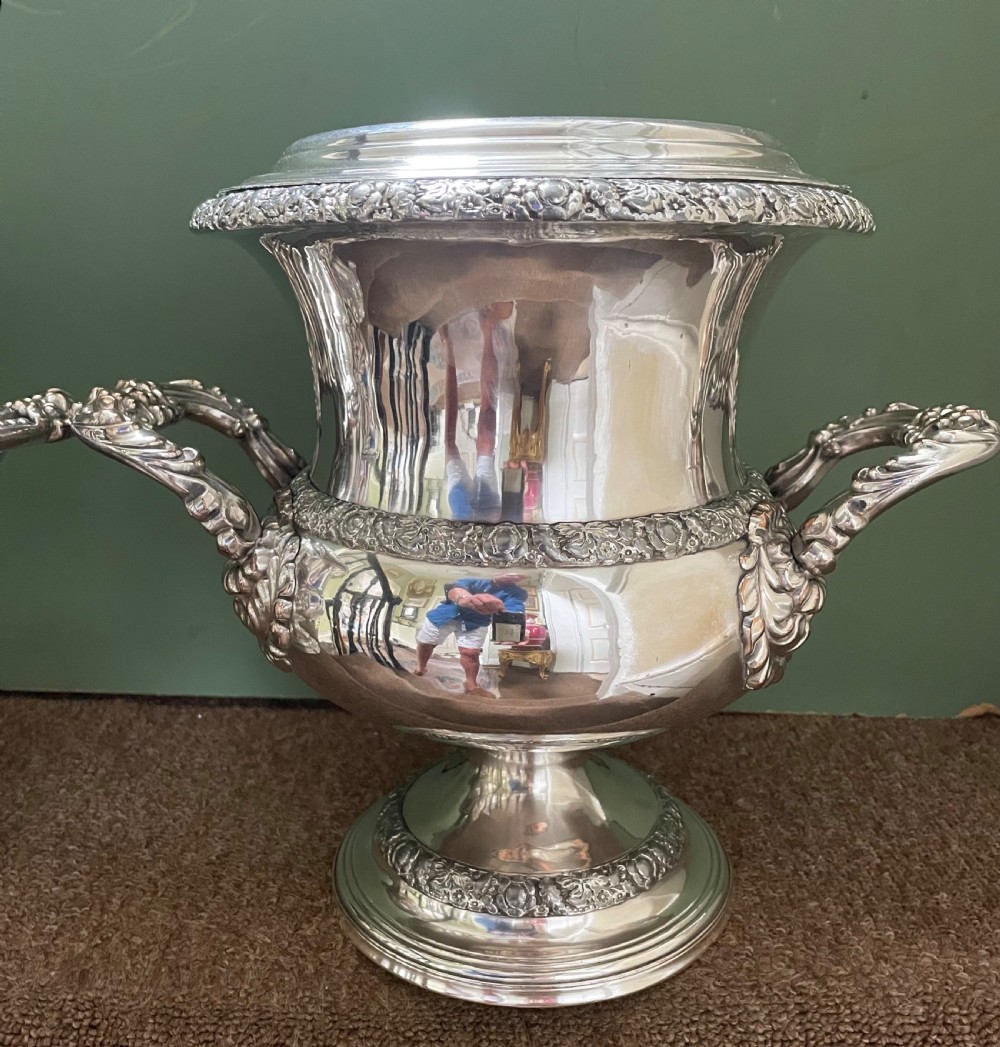 A pair of polished silver-plated campana-form wine coolers featuring ornate foliate handles, intricate relief borders, and pedestal bases. View VII