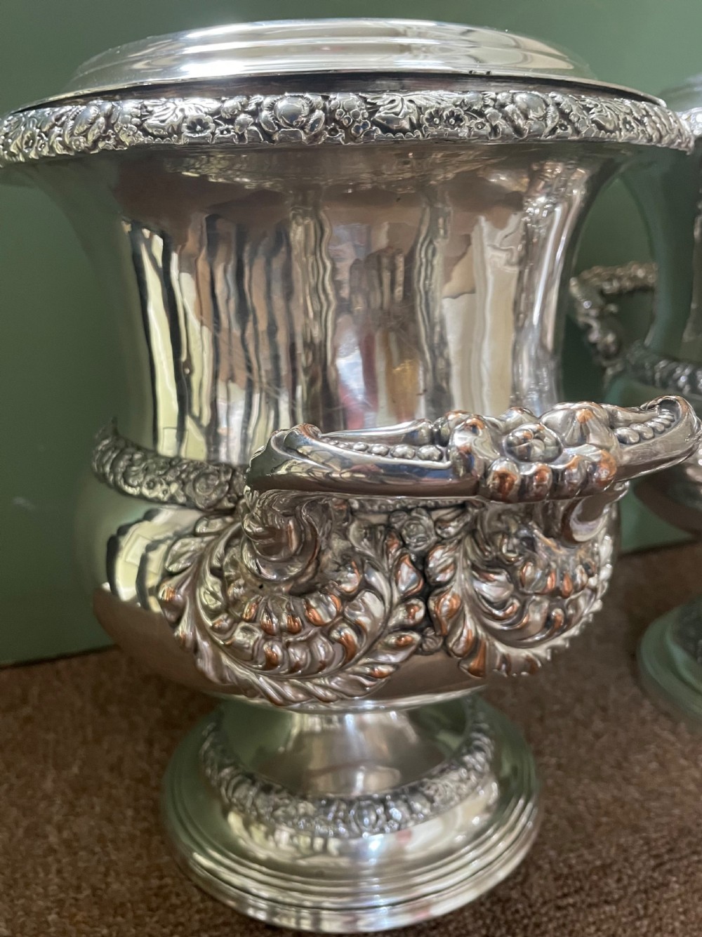 A pair of polished silver-plated campana-form wine coolers featuring ornate foliate handles, intricate relief borders, and pedestal bases. View VIII