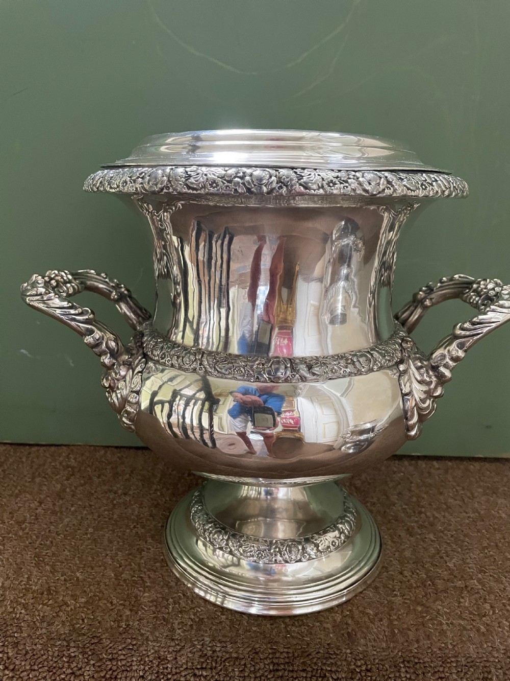 A pair of polished silver-plated campana-form wine coolers featuring ornate foliate handles, intricate relief borders, and pedestal bases. View X