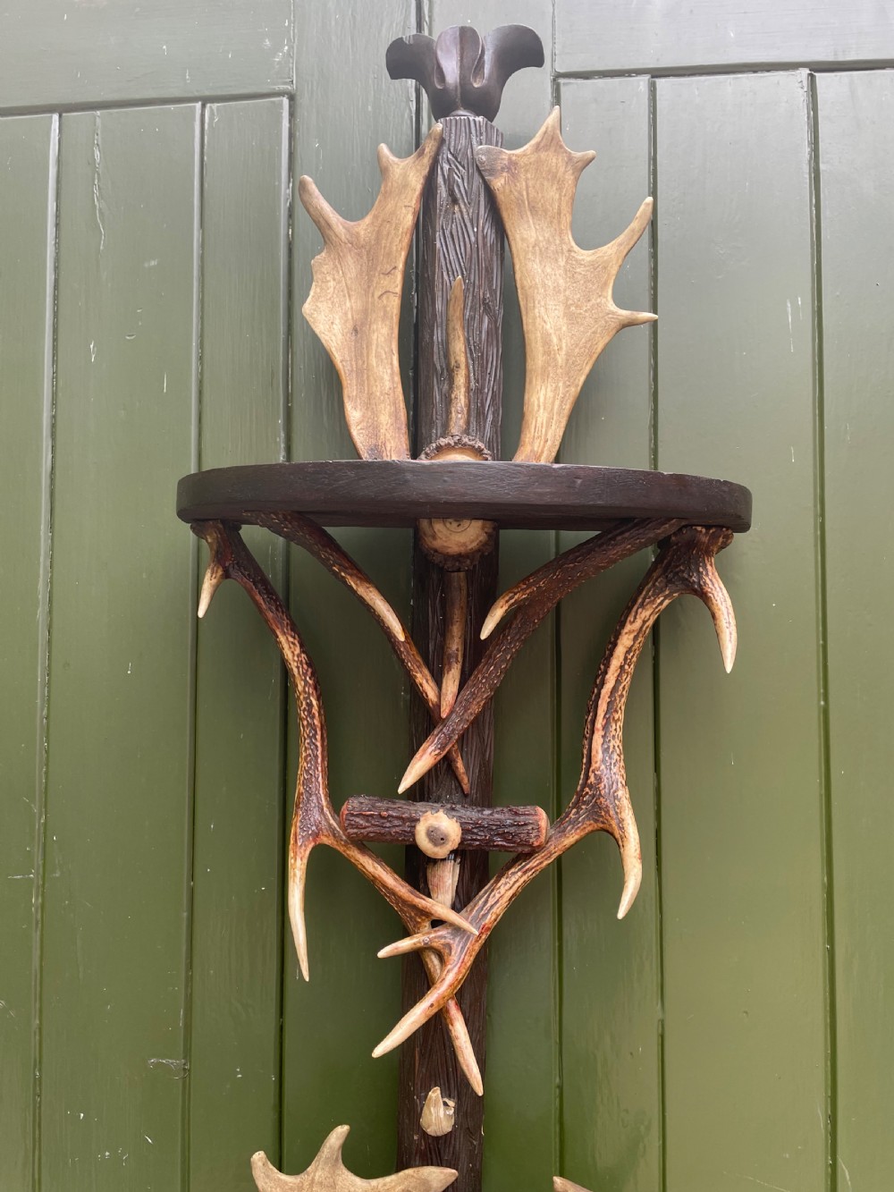 A nineteenth-century Black Forest carved wood wall rack with natural deer antlers, small shelves, and coat hooks against a green background. View III