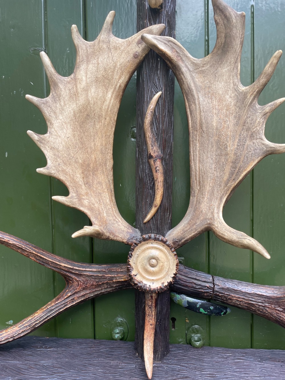 A nineteenth-century Black Forest carved wood wall rack with natural deer antlers, small shelves, and coat hooks against a green background. View VII