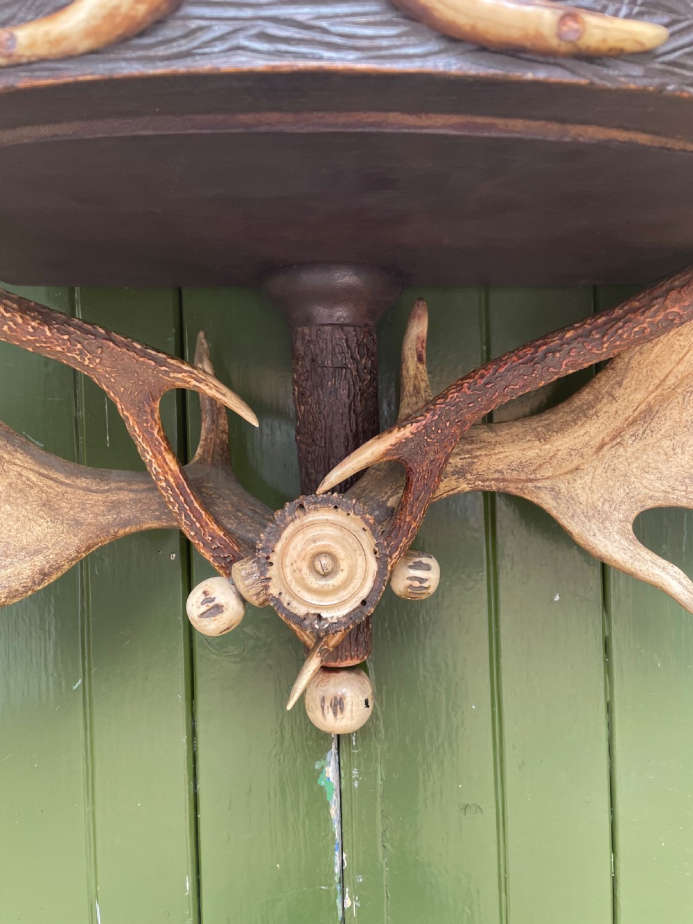 A nineteenth-century Black Forest carved wood wall rack with natural deer antlers, small shelves, and coat hooks against a green background. View VIII