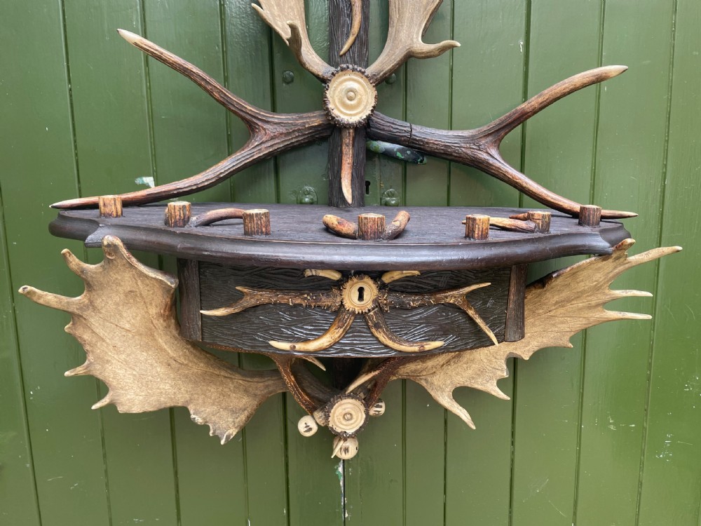 A nineteenth-century Black Forest carved wood wall rack with natural deer antlers, small shelves, and coat hooks against a green background. View XIV