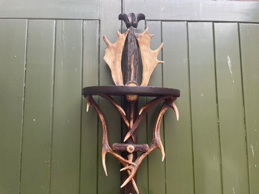 A nineteenth-century Black Forest carved wood wall rack with natural deer antlers, small shelves, and coat hooks against a green background. View XVI