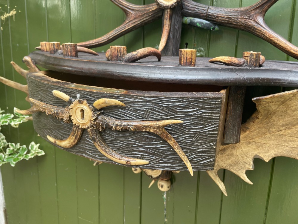 A nineteenth-century Black Forest carved wood wall rack with natural deer antlers, small shelves, and coat hooks against a green background. View XIX