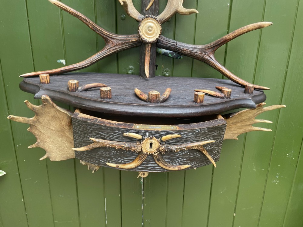 A nineteenth-century Black Forest carved wood wall rack with natural deer antlers, small shelves, and coat hooks against a green background. View XX
