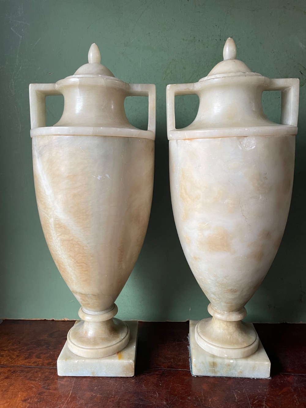 A pair of early nineteenth-century carved cream alabaster classical urns with lids, angular side handles, and square pedestal bases.