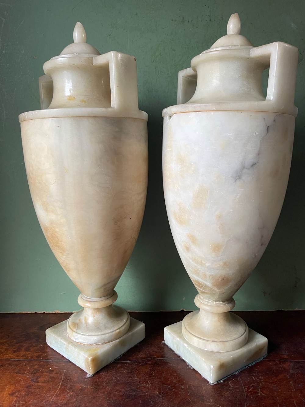 A pair of early nineteenth-century carved cream alabaster classical urns with lids, angular side handles, and square pedestal bases. View V