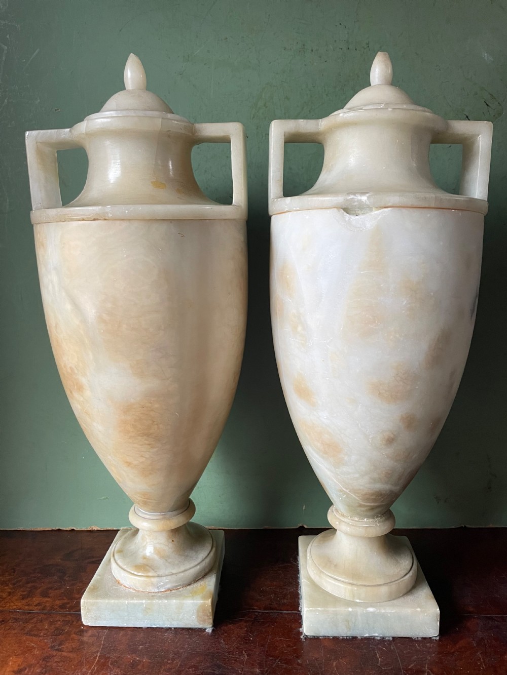 A pair of early nineteenth-century carved cream alabaster classical urns with lids, angular side handles, and square pedestal bases. View VI