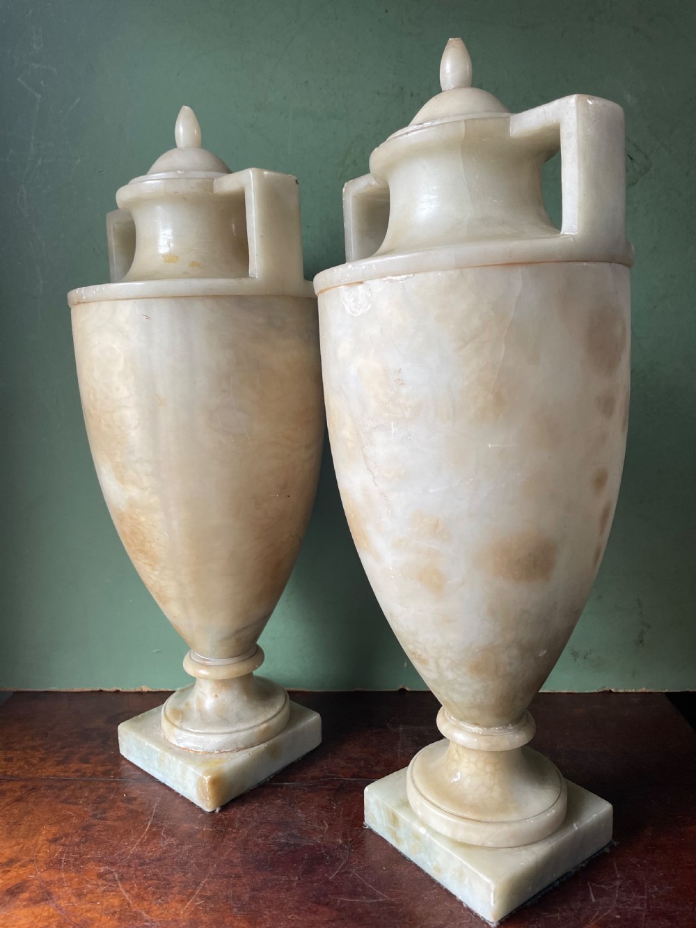 A pair of early nineteenth-century carved cream alabaster classical urns with lids, angular side handles, and square pedestal bases. View XIII