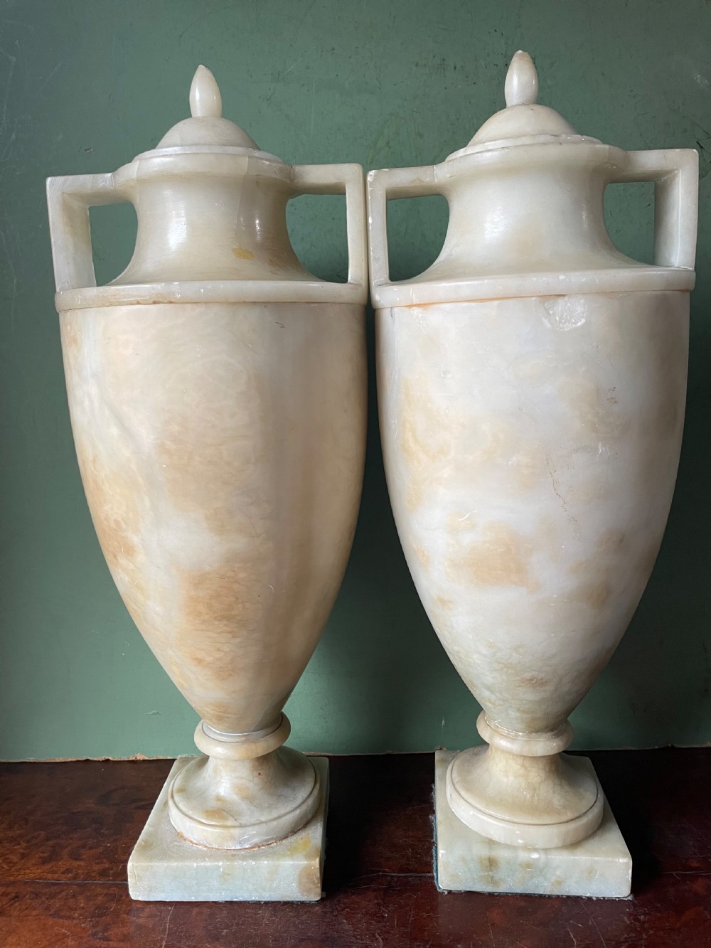 A pair of early nineteenth-century carved cream alabaster classical urns with lids, angular side handles, and square pedestal bases. View XIV