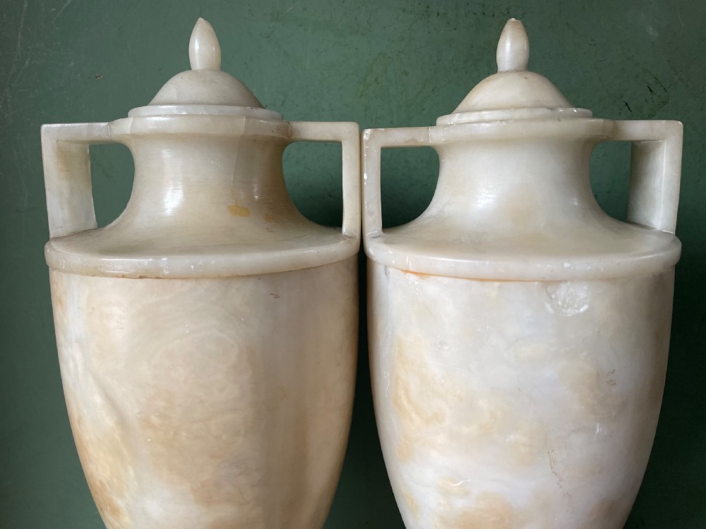 A pair of early nineteenth-century carved cream alabaster classical urns with lids, angular side handles, and square pedestal bases. View XV