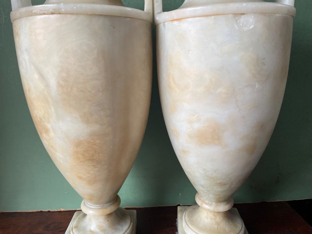 A pair of early nineteenth-century carved cream alabaster classical urns with lids, angular side handles, and square pedestal bases. View XVI