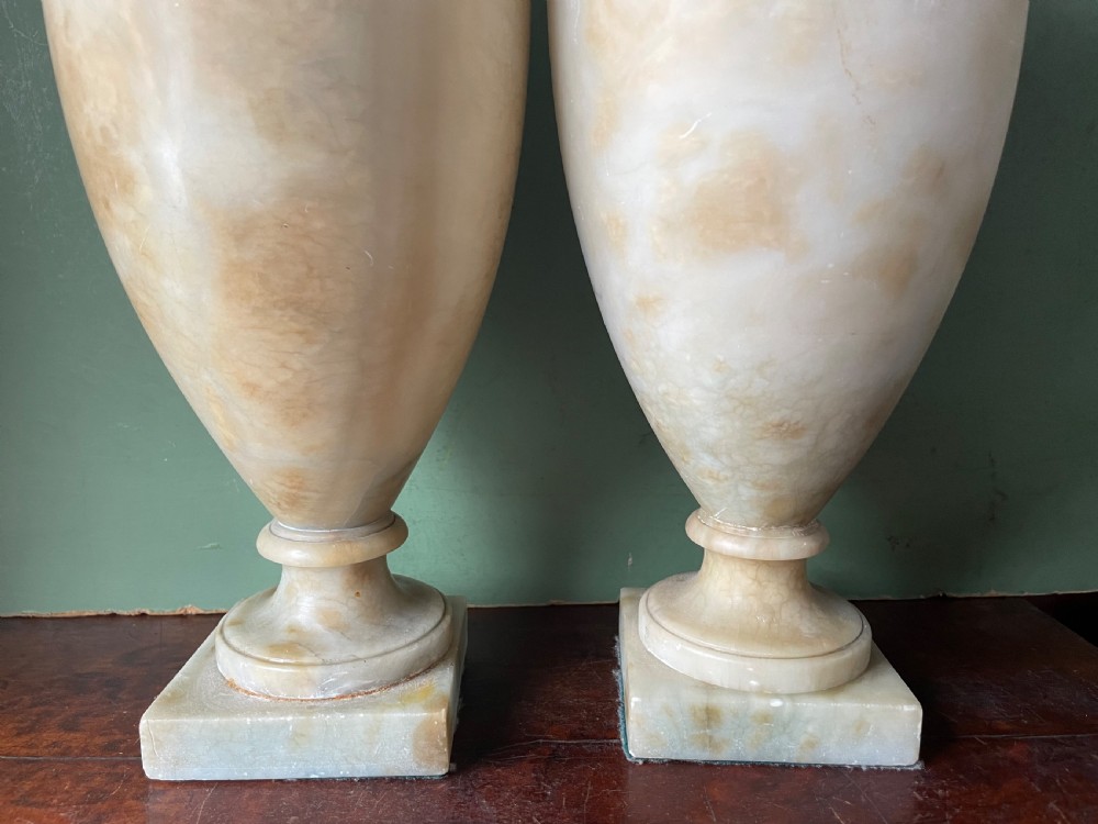 A pair of early nineteenth-century carved cream alabaster classical urns with lids, angular side handles, and square pedestal bases. View XVII