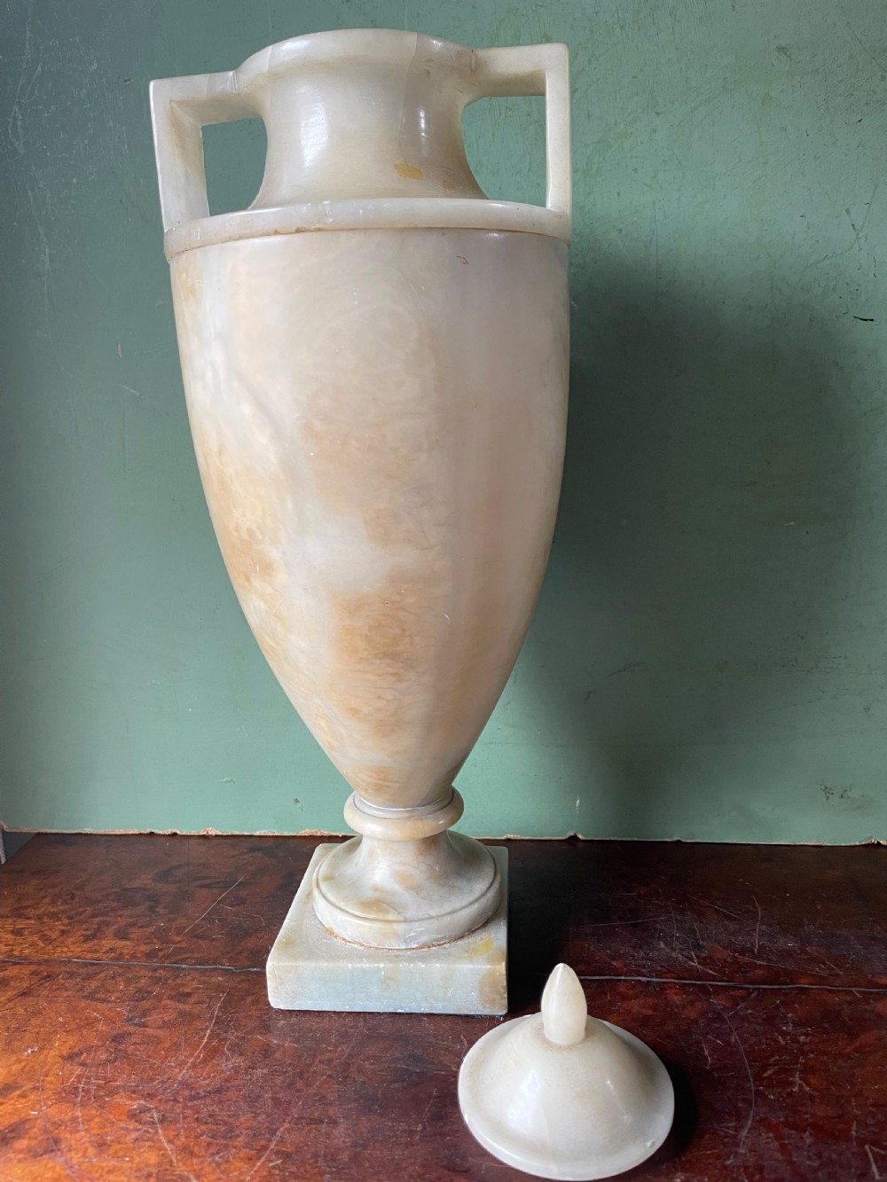 A pair of early nineteenth-century carved cream alabaster classical urns with lids, angular side handles, and square pedestal bases. View XVIII
