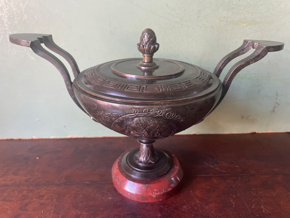 A nineteenth-century bronze lidded tazza featuring Greek key chasing and elevated handles, supported by a round red marble base.