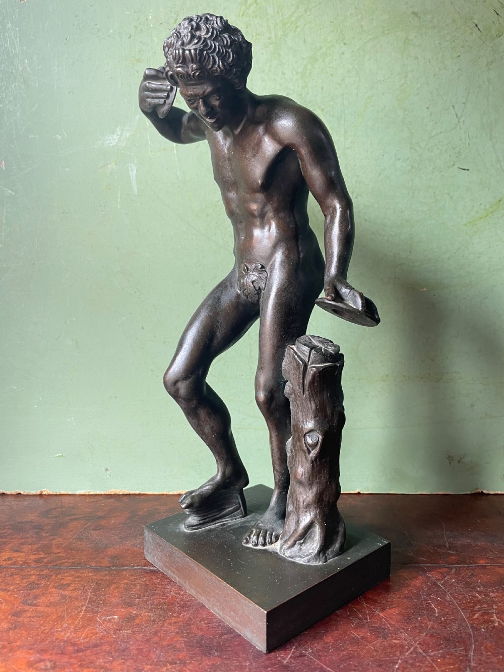 A dark patinated bronze sculpture depicting the classical figure of the Dancing Faun holding cymbals, mounted on a rectangular metal plinth. View III
