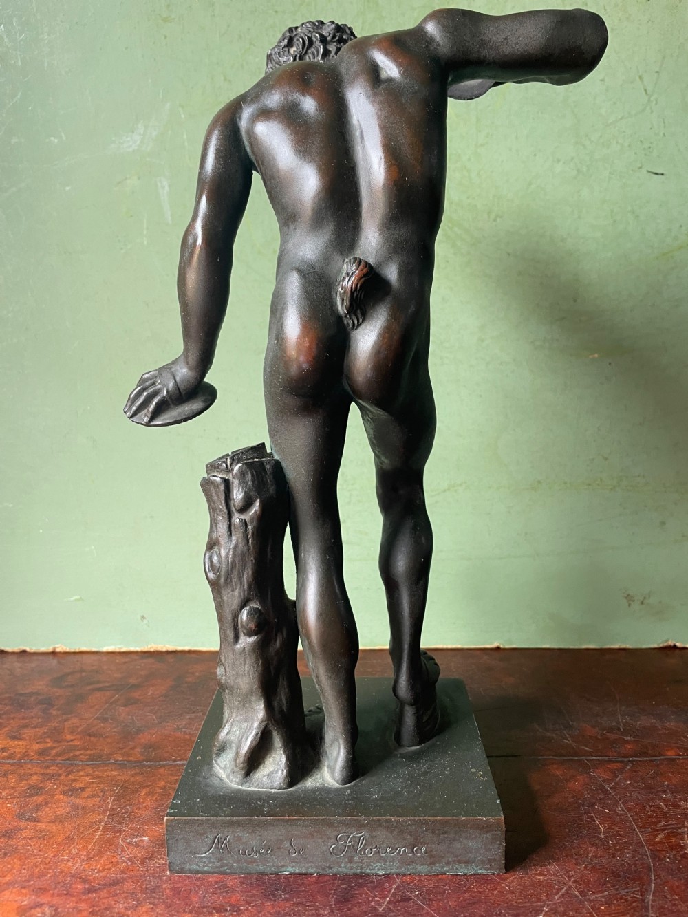 A dark patinated bronze sculpture depicting the classical figure of the Dancing Faun holding cymbals, mounted on a rectangular metal plinth. View VI