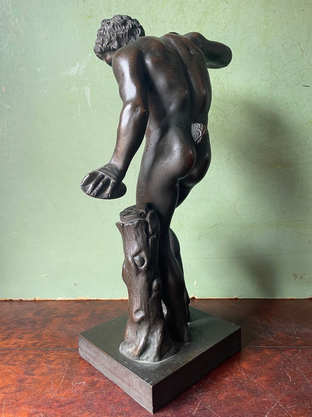 A dark patinated bronze sculpture depicting the classical figure of the Dancing Faun holding cymbals, mounted on a rectangular metal plinth. View VII