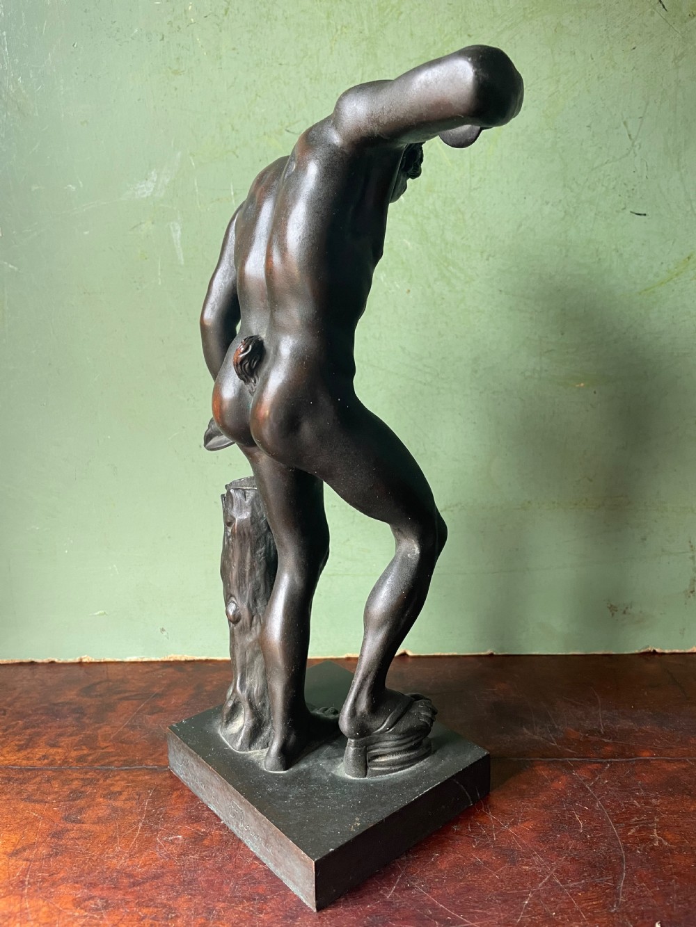 A dark patinated bronze sculpture depicting the classical figure of the Dancing Faun holding cymbals, mounted on a rectangular metal plinth. View X