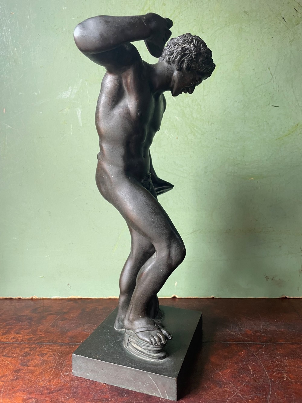 A dark patinated bronze sculpture depicting the classical figure of the Dancing Faun holding cymbals, mounted on a rectangular metal plinth. View XI