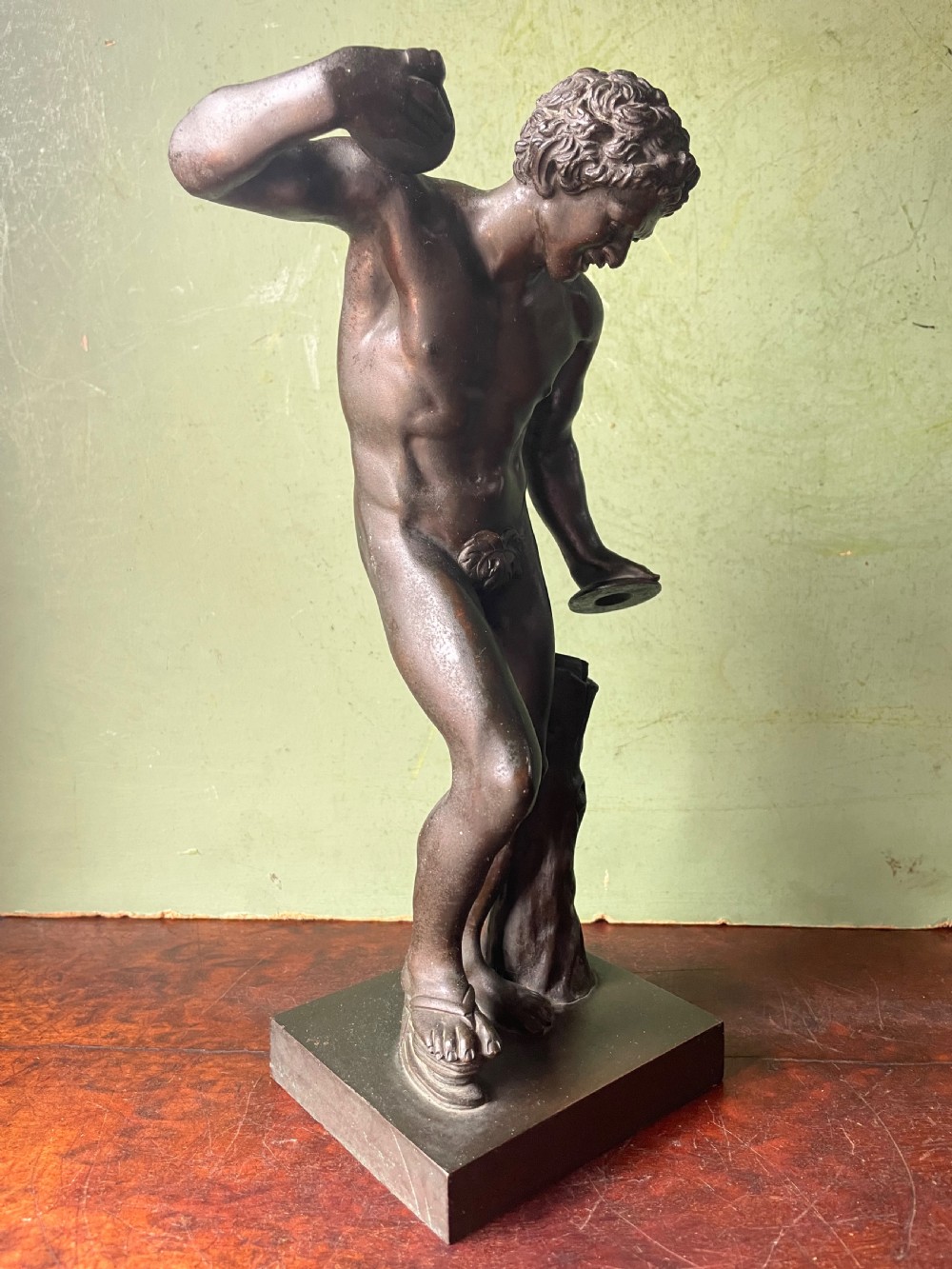 A dark patinated bronze sculpture depicting the classical figure of the Dancing Faun holding cymbals, mounted on a rectangular metal plinth. View XII