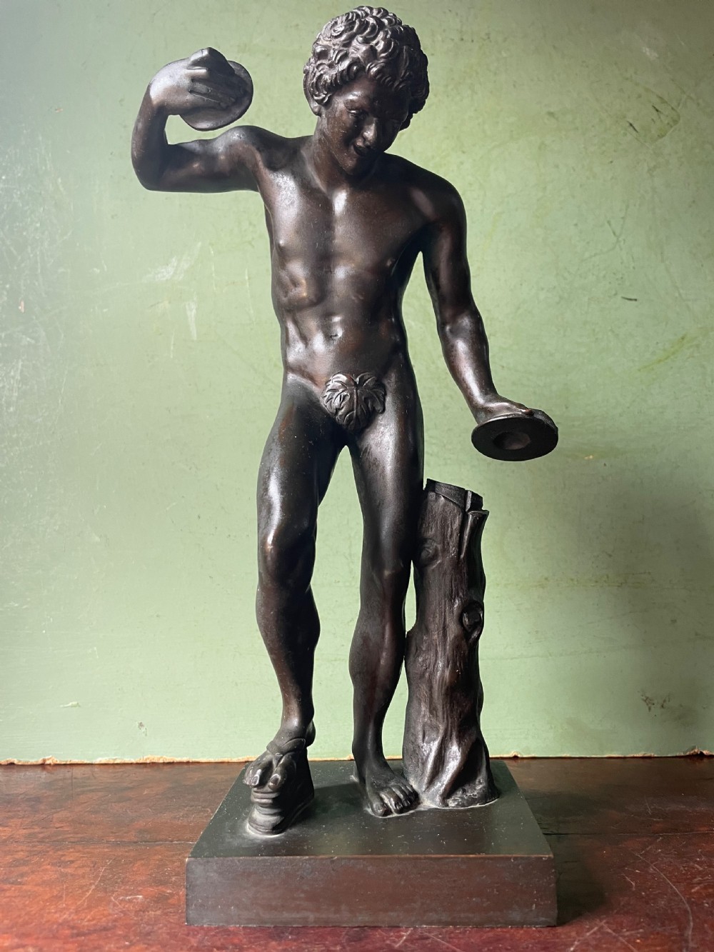A dark patinated bronze sculpture depicting the classical figure of the Dancing Faun holding cymbals, mounted on a rectangular metal plinth. View XIV