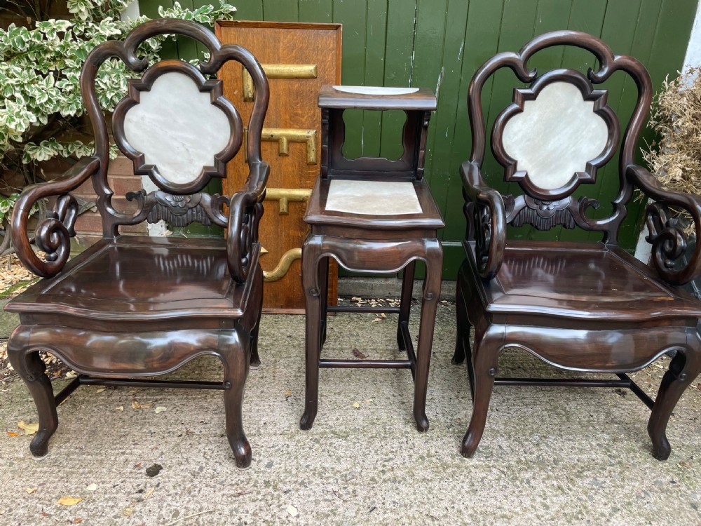 A pair of late Qing Dynasty dark hardwood armchairs with circular marble splat inlays flanking a matching two-tier stand.