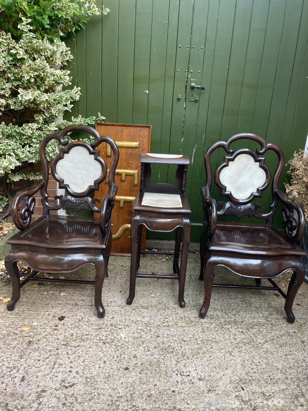 A pair of late Qing Dynasty dark hardwood armchairs with circular marble splat inlays flanking a matching two-tier stand. View II