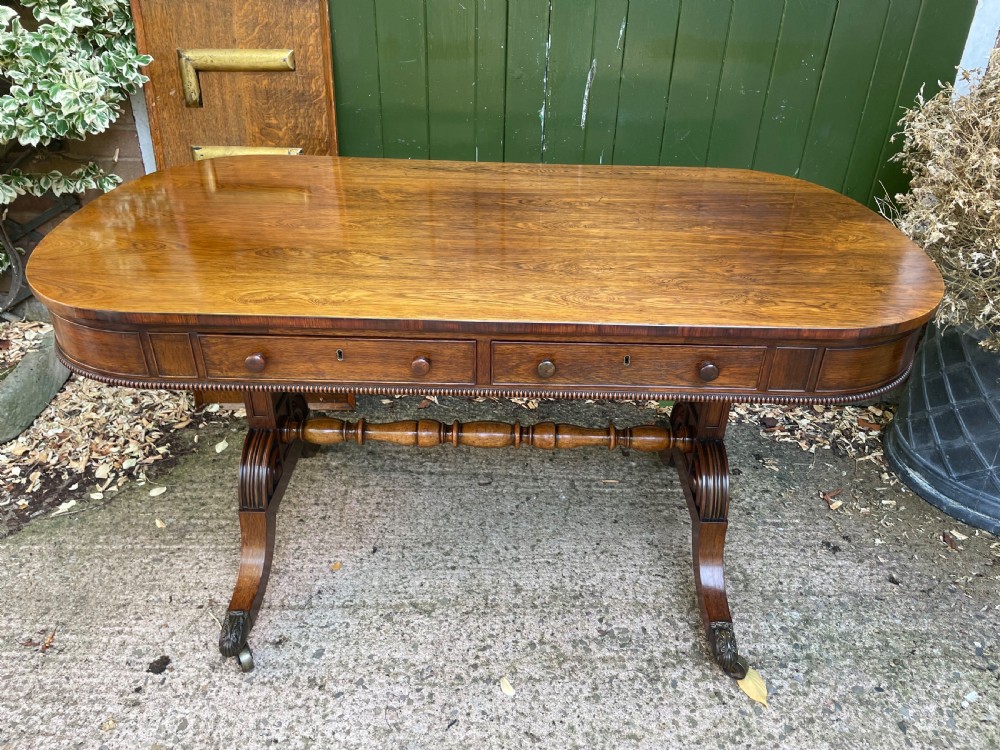 An early nineteenth-century George IV rosewood library table featuring two frieze drawers, a turned horizontal stretcher, and trestle legs on brass castors.
