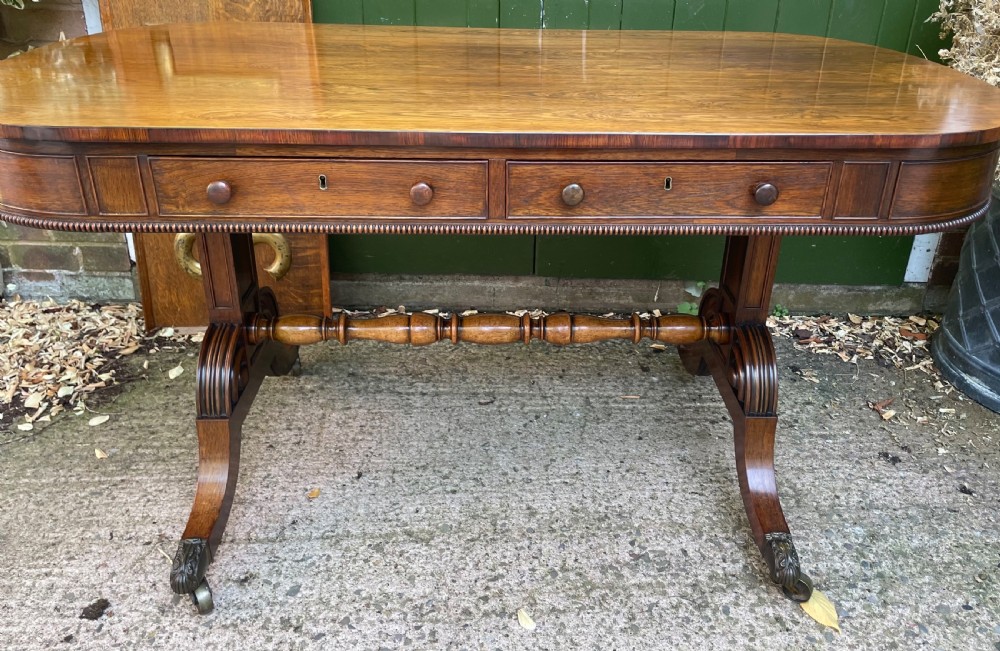An early nineteenth-century George IV rosewood library table featuring two frieze drawers, a turned horizontal stretcher, and trestle legs on brass castors. View II