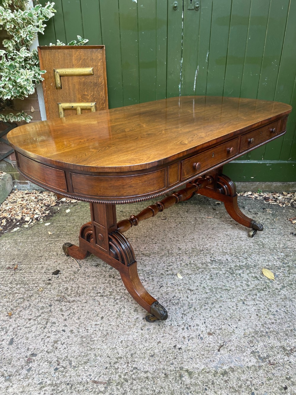 An early nineteenth-century George IV rosewood library table featuring two frieze drawers, a turned horizontal stretcher, and trestle legs on brass castors. View III