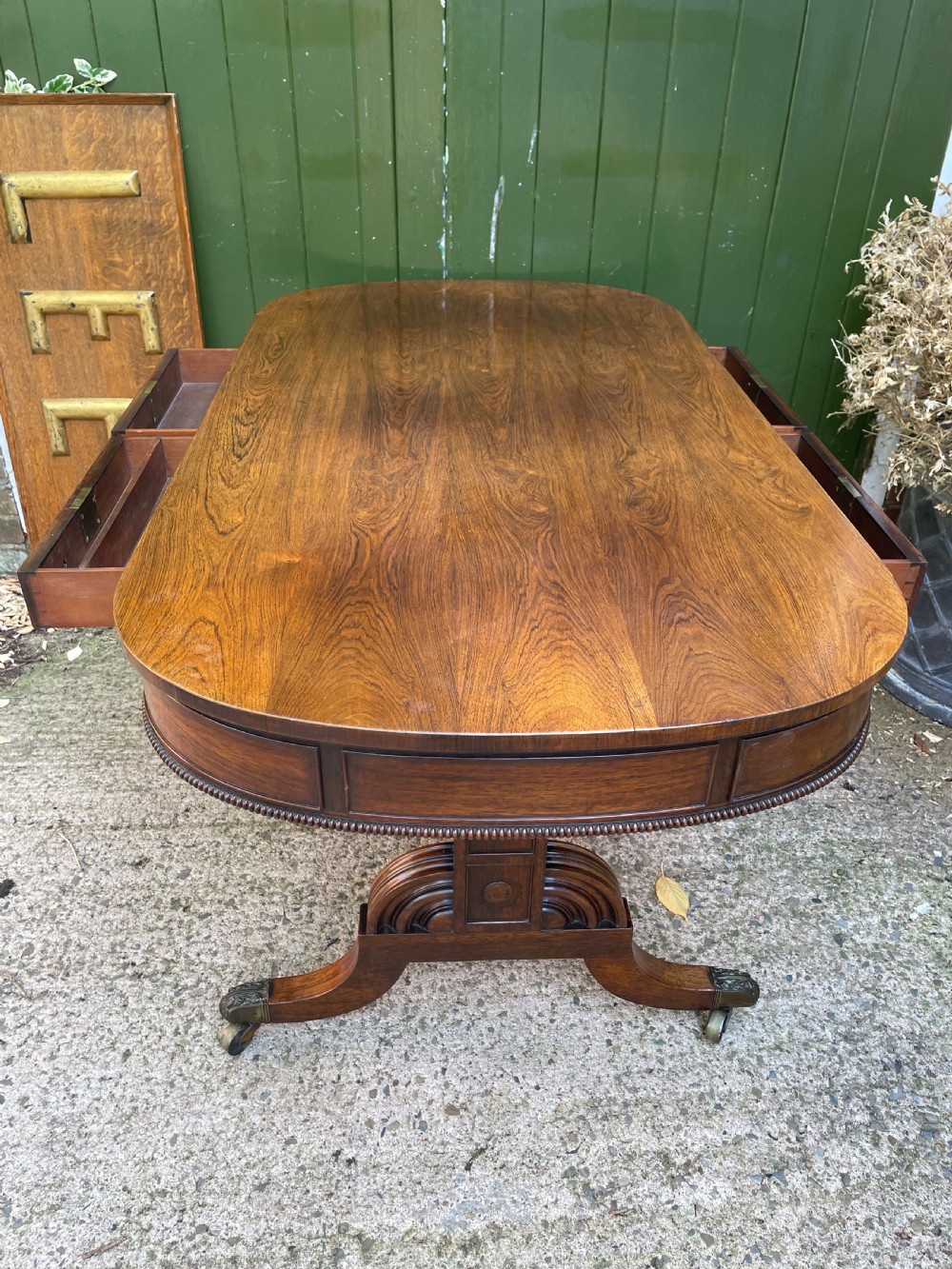 An early nineteenth-century George IV rosewood library table featuring two frieze drawers, a turned horizontal stretcher, and trestle legs on brass castors. View IX
