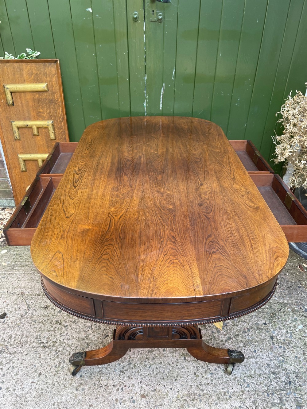 An early nineteenth-century George IV rosewood library table featuring two frieze drawers, a turned horizontal stretcher, and trestle legs on brass castors. View XI