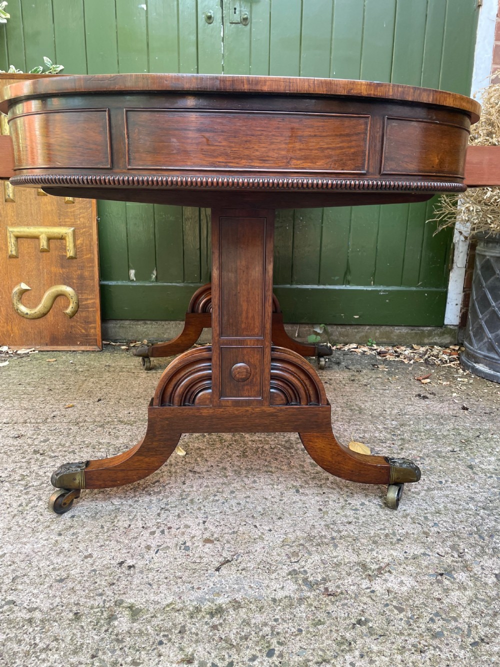 An early nineteenth-century George IV rosewood library table featuring two frieze drawers, a turned horizontal stretcher, and trestle legs on brass castors. View XII