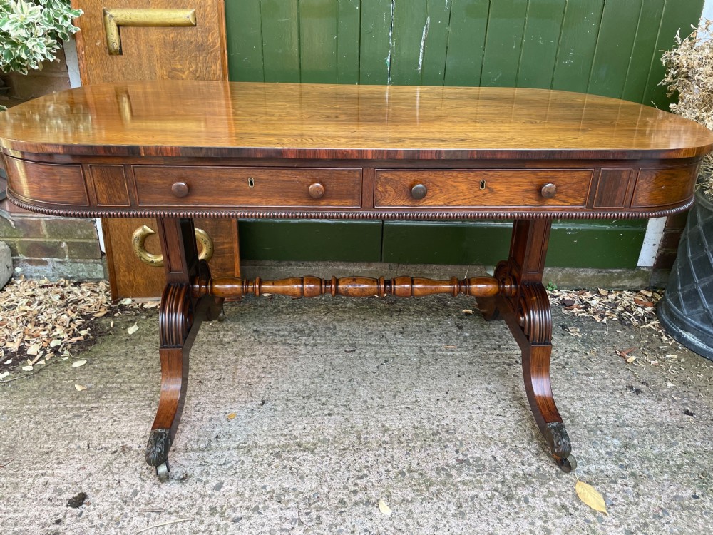 An early nineteenth-century George IV rosewood library table featuring two frieze drawers, a turned horizontal stretcher, and trestle legs on brass castors. View XV
