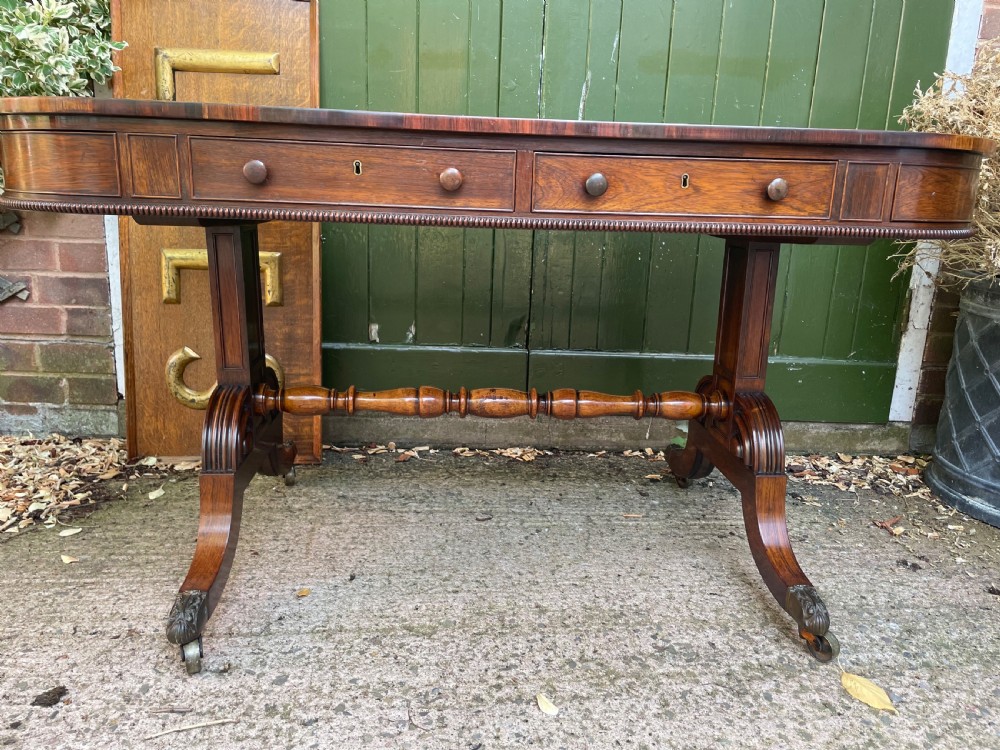 An early nineteenth-century George IV rosewood library table featuring two frieze drawers, a turned horizontal stretcher, and trestle legs on brass castors. View XVI