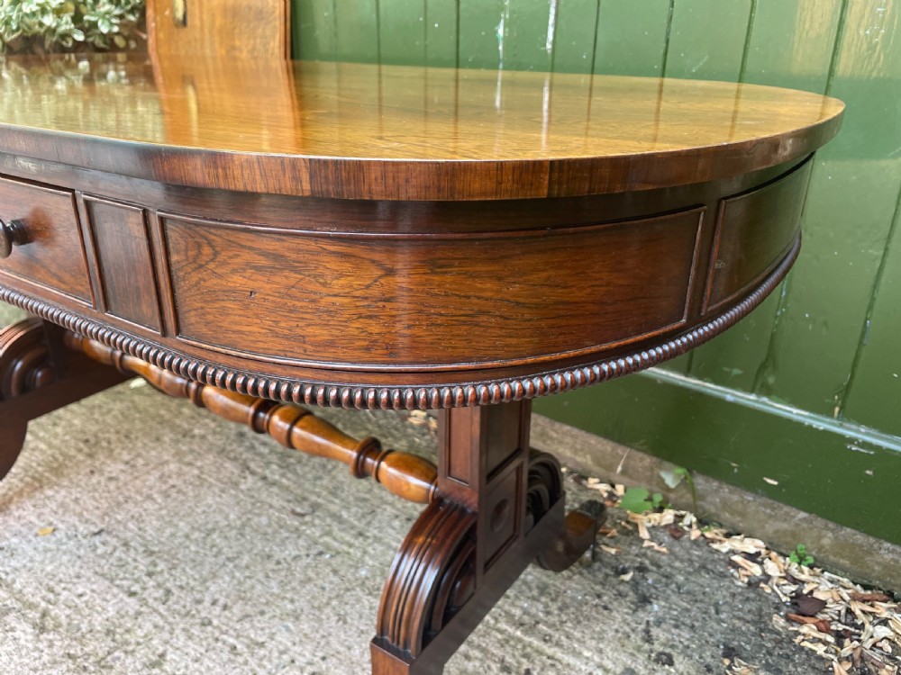 An early nineteenth-century George IV rosewood library table featuring two frieze drawers, a turned horizontal stretcher, and trestle legs on brass castors. View XVIII